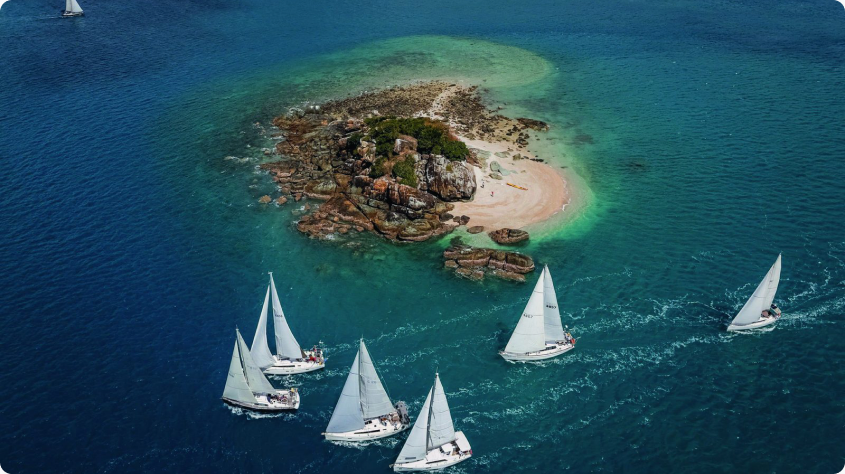 Aerial view of yachts racing past a small island in the Whitsundays